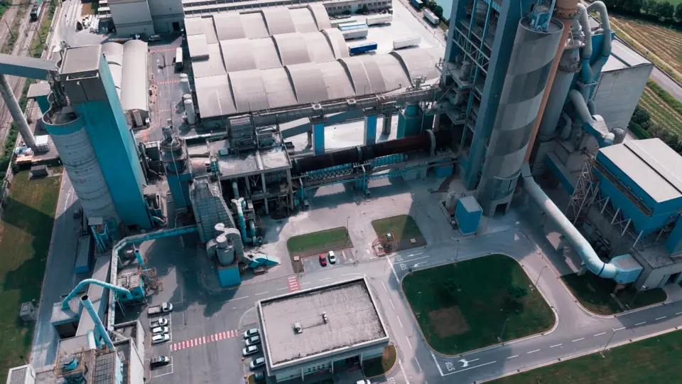 An aerial view of an industrial site with large concrete structures and machinery, surrounded by green spaces and roads.