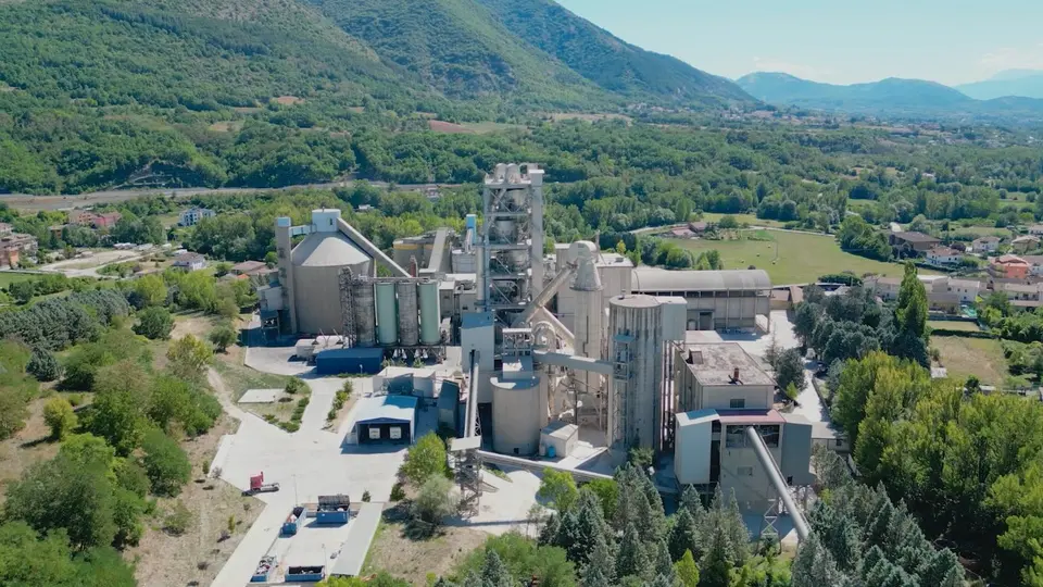 Un impianto industriale per la produzione di cemento circondato da colline verdeggianti e alberi.