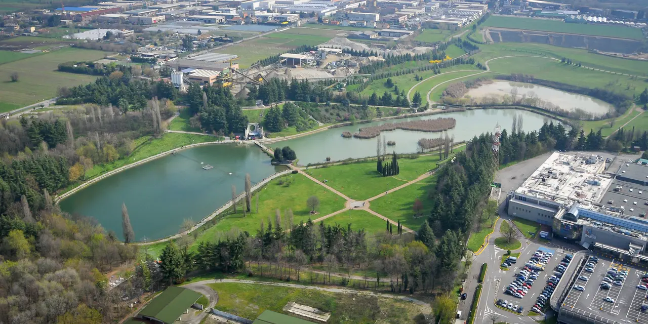 Vista aerea di un sito industriale circondato da aree verdi e laghi in un contesto urbano.