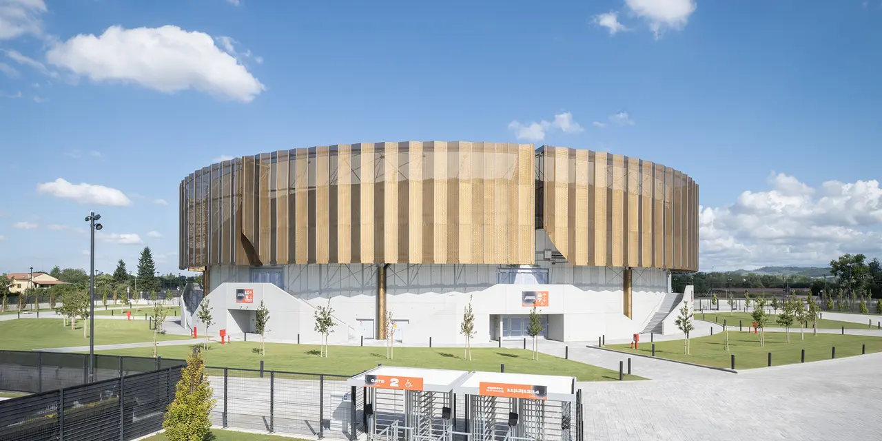 Edificio industriale moderno con facciata circolare rivestita in legno, circondato da aree verdi.