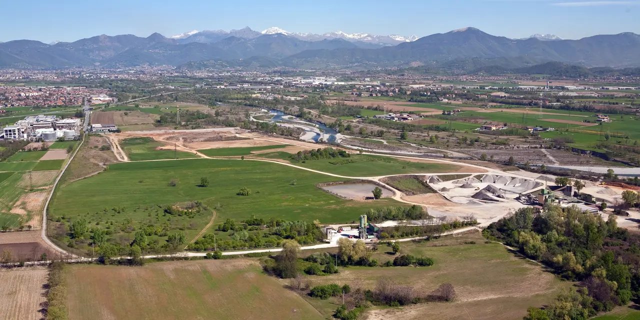 Vista aerea di un sito industriale circondato da campi e montagne in lontananza.
