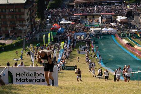 Evento sportivo all'aperto con persone che risalgono una collina, visibile un cartello di Heidelberg Materials in primo piano.
