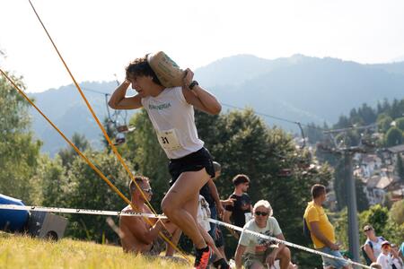 Un uomo corre in una competizione trasportando un sacco di cemento su una collina verde.