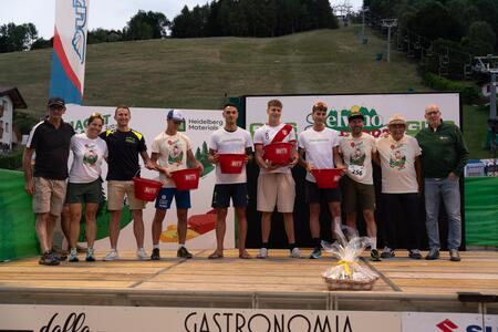 Un gruppo di persone in posa su un palco all'aperto, con magliette coordinate e contenitori rossi in mano.