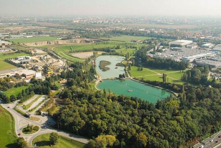 Vista aerea di un'area industriale e urbana con un grande parco verde e un lago in primo piano.