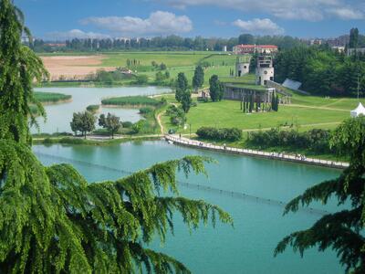 Vista di un paesaggio verde con un lago e strutture storiche sullo sfondo.