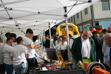 Persone partecipano a un evento aziendale all'aperto con stand informativi sotto tendoni bianchi.
