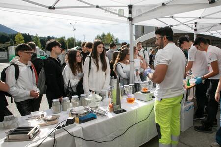 Persone riunite sotto un gazebo osservano una dimostrazione di materiali da costruzione.