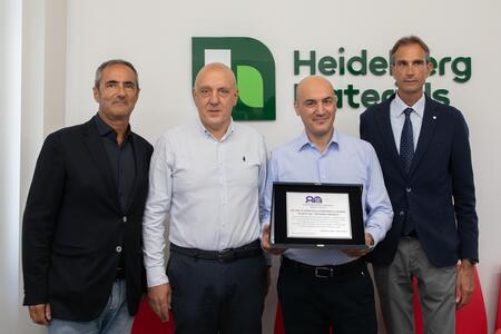 Quattro uomini in posa davanti al logo di Heidelberg Materials, uno di loro tiene un certificato.