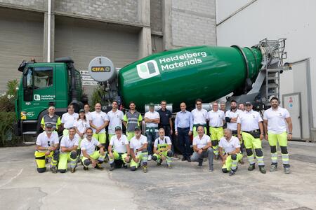 Un gruppo di lavoratori in posa davanti a un camion betoniera verde con il logo di Heidelberg Materials.