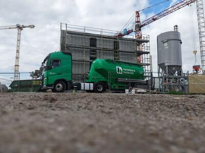 Camion Heidelberg Materials presso un cantiere con strutture in costruzione e gru visibili.