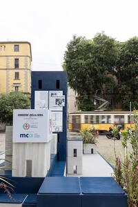 Installazione di modelli architettonici moderni in un contesto urbano con un tram giallo sullo sfondo.